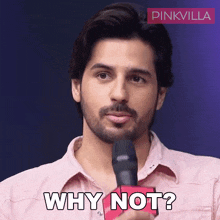 a man in a pink shirt is holding a microphone and saying why not