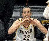 a woman wearing a fever 22 jersey makes a heart with her hands