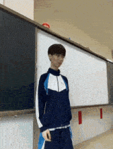 a young man in a blue and white tracksuit stands in front of a white board