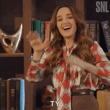 a woman is standing in front of a bookshelf and smiling while saying ty .