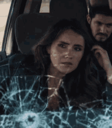 a man and a woman are sitting in a car with a bullet hole in the window