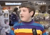 a young boy wearing a striped sweater is talking into a microphone in a store .