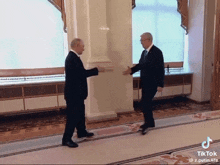 two men in suits are shaking hands in a hallway with tiktok written on the bottom
