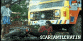 a man is laying on the ground in front of a yellow truck that says ' tentkotta ' on it