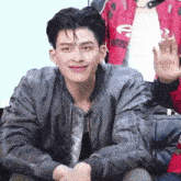 a young man wearing a gray jacket is smiling and waving while sitting down .