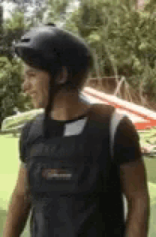 a man wearing a helmet and a black shirt is standing in front of a green field .