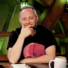 a man is sitting at a table with his hands on his chin