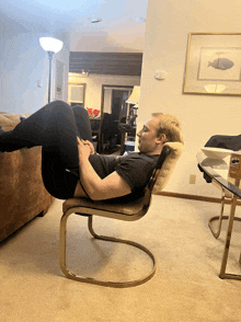 a man sits in a chair with his legs crossed in front of a picture of a fish on a wall