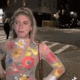 a woman wearing a floral shirt is standing on a sidewalk in front of a street .