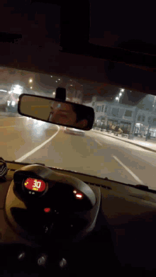 a car is driving down a street at night and the rear view mirror shows a man 's face