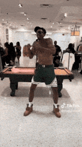 a man without a shirt is dancing in front of a pool table