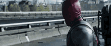 a man in a deadpool costume is standing on a bridge looking out over a city .