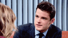 a man in a suit and tie is talking to a woman on a couch