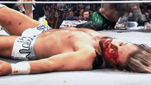 a wrestler with blood on his face is laying on the ground in a wrestling ring