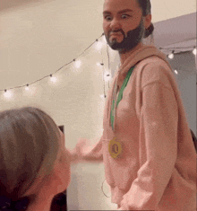 a man with a beard and a medal around his neck is wearing a pink sweatshirt