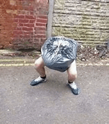 a person is squatting with a trash bag on their head .