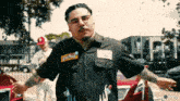 a man wearing glasses and a shirt that says staff is standing with his arms outstretched in front of a red car .