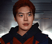 a man with red hair is wearing a black hoodie and a red jacket