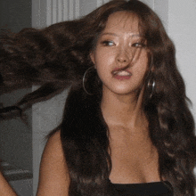 a woman wearing hoop earrings and a black top has her hair blowing in the wind