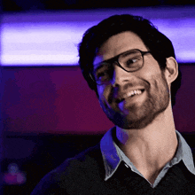 a man with glasses and a beard smiles in front of purple lights