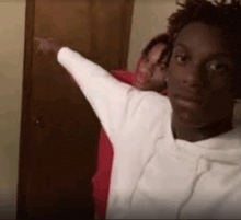 a man in a white hoodie is pointing at a door while another man in a red hoodie looks on .
