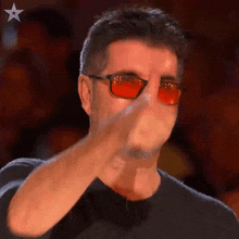a man wearing red sunglasses and a black shirt is covering his mouth with his hand .
