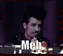 a man sitting in front of a microphone with the word meh on the screen