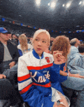 a woman wearing a knicks jacket sits in a crowd