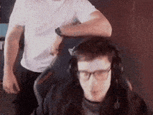 a man wearing headphones and glasses is sitting in a chair with a man standing behind him .