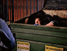 a man is laying in a dumpster that has a caution sign on it