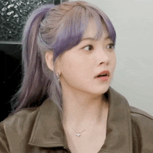 a woman with purple hair is wearing a leather jacket and a necklace with a heart on it