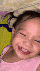 a baby girl in a pink tank top smiles with her eyes closed