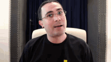 a man wearing glasses and a black shirt has a yellow sticker on his shirt