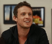 a man in a black shirt is smiling in front of a picture that says ' a ' on it