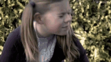 a young girl with pigtails is making a funny face while standing in front of a bush .