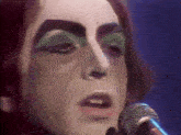a close up of a person singing into a microphone with green makeup on their face