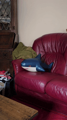 a red leather couch with a blue shark pillow on it