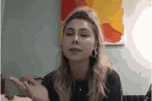 a woman is sitting at a table with a painting on the wall behind her
