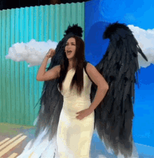 a woman in a white dress with black wings is standing in front of a blue wall
