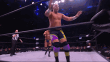 a wrestler in purple shorts and yellow knee pads stands in the ring