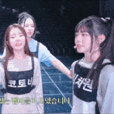 a girl wearing a vest with korean writing on it stands next to another girl