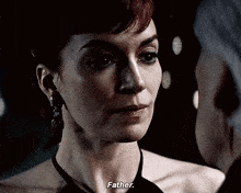 a woman in a black dress is talking to a man in a dark room and says father .