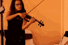 a woman is playing a violin in front of an orange wall
