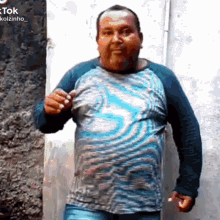 a man in a blue shirt is standing in front of a wall and holding his shirt up .