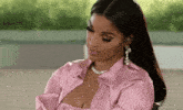 a woman wearing a pink shirt and a necklace is sitting down .