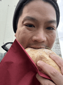 a man is eating a sandwich with a red napkin covering his mouth