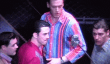 a group of men are standing in a dark room and one of them is holding a microphone