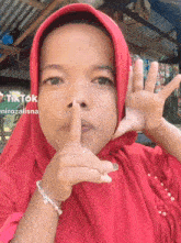a girl wearing a red hijab and a bracelet holds her finger to her mouth
