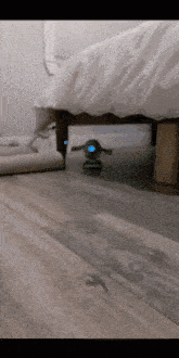 a green robot is sitting under a bed with a blue light on it
