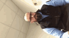a man with glasses and a beard is wearing a blue shirt and a black vest .